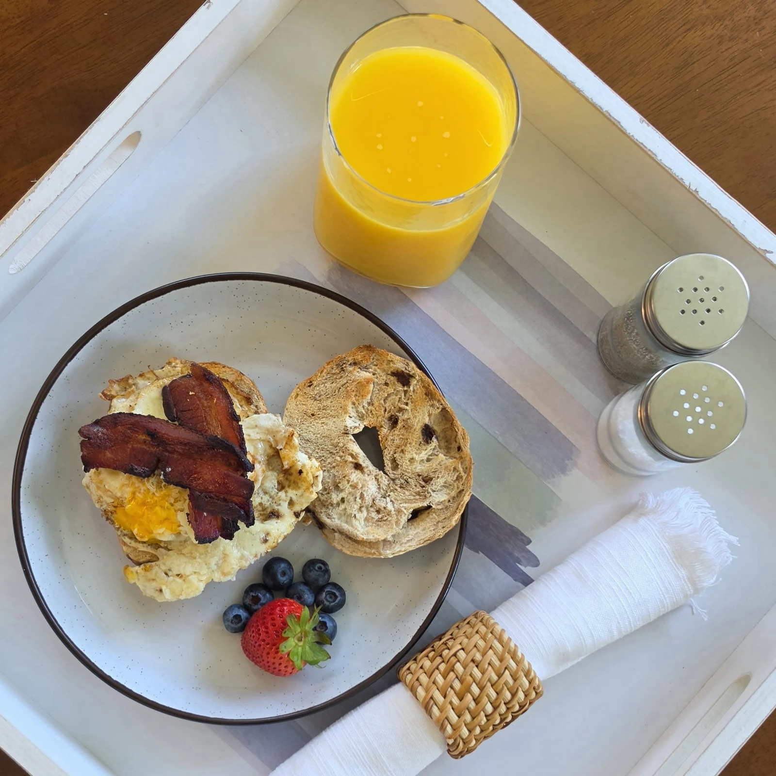 Open bacon, egg and sharp cheddar sandwich on a toasted cinnamon raisin bagel with berries and orange juice